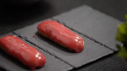 Pink glaze eclair on stone plates. Modern desserts and cakes. Cupcakes with cream filling. Professional pastry.