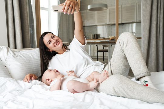 Image of cheerful mother taking selfie photo with her baby on cellphone