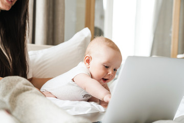 Photo of nice family mother and baby playing with laptop on bed