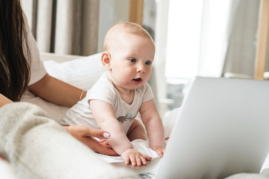 Photo of nice family mother and baby playing with laptop on bed
