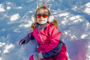 Young girl with sunglasses sitting on the snow place. Winter time
