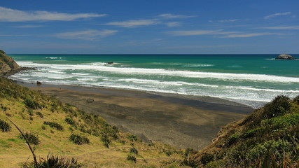 Scenic view on a beautiful summer day of waves breaking and the black sand beach at Maori Bay, Muriwai Beach, on the west coast of Auckland, New Zealand