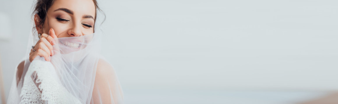 Horizontal crop of young bride with closed eyes holding veil
