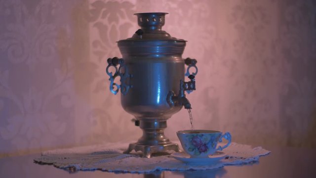 Pouring Hot Water from a Soviet Vintage Samovar Electric Metal Tea Kettle into a Gorgeous Cup. Red Lighting On Ornamented Wallpaper