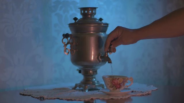 Pouring Hot Water from a Soviet Vintage Samovar Electric Metal Tea Kettle into a Gorgeous Cup. Blue Lighting On Ornamented Wallpaper