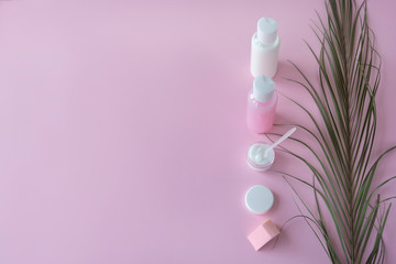 Bottles and container for cosmetic products with green herbal leaves, packaging with blank labels for branding. Pink background, copy space, natural organic cosmetic products concept