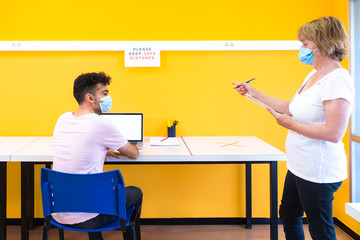 Teacher and student with a medical face masks at school. Doing class in the new normal during the coronavirus pandemic with the necessary preventive measures and maintaining the safety distance.