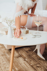 Selective focus of bride in bra and veil touching accessories near wine and perfume on coffee table