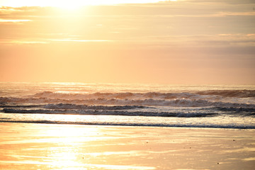 Golden sunrise in the early morning by the ocean. Waves and sandy beach. Minimalistic marine look. Atlantic Ocean.
