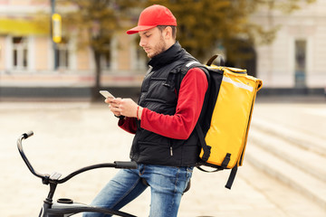 Courier Texting On Smartphone Sitting On Bicycle Delivering Lunches Outdoor