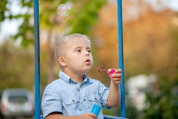 The daily life of a child with disabilities. A boy with Down syndrome blows soap bubbles....