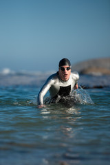 Athlete in wetsuit emerging from the ocean after a swim.