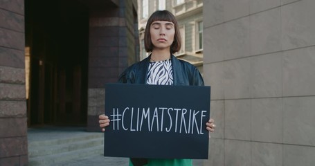 Millennial woman holding placard with climate strike hashtag while standing at street. Hipster girl striking for ecology and clean planet. Concept of eco and save Earth. Zoom in