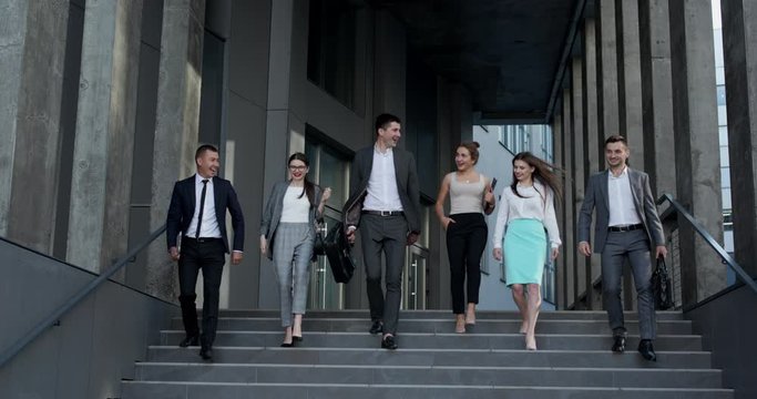Confident team members walking on stairs. Business men and women in formal suits go and talk on the background of modern office building