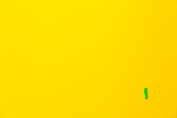 Number 1, one, the first of the plastic baby green toy number is located in the lower right corner on a yellow paper background. Banner on the topic of page numbering, timing or day in the calendar