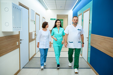 Three smiling doctors walking in clinic corridor