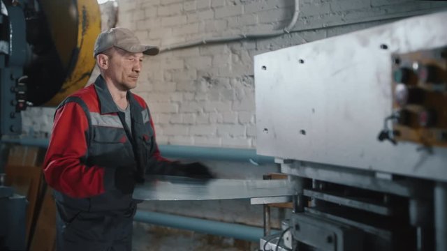 Professional caucasian engineer works with a sheet of metal on a machine tool. Master, locksmith in production. Machine tools for metal working. Manual and automated work in the factory.
