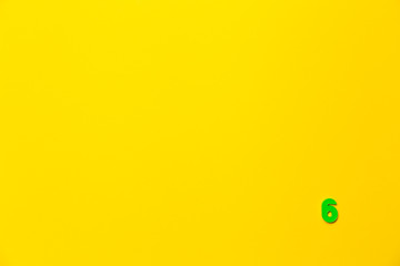 Number 6, six, the sixth of the plastic baby green toy number is located in the lower right corner on a yellow paper background. Banner on the topic of page numbering, timing or day in the calendar