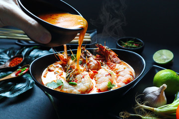 tom yam kung soup with shrimp and prawn are served on the black table with other ingredients, chilli, lemongrass, garlic, tomato, lime in the Thai restaurant