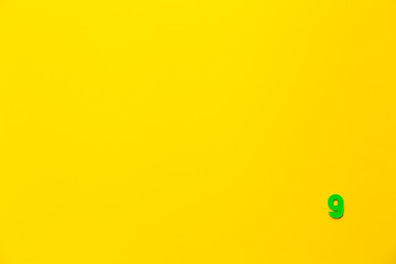 Number 9, nine, the ninth of the plastic baby green toy number is located in the lower right corner on a yellow paper background. Banner on the topic of page numbering, timing or day in the calendar