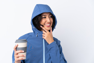 Mixed race woman wearing winter clothes with the hood on and holding a hot takeaway coffee over isolated white background thinking an idea and looking side