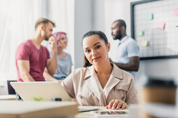 Selective focus of businesswoman looking at camera near managers at background in office