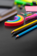 Back to school concept. Colorful pencils, rainbow eraser, notebook, sticky notes and office supplies on black background. Copy space.