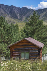 Fototapeta na wymiar A small log house for tourists stands against the backdrop of the mountain slopes. Travel through the Altai Republic in Russia in the summer months.