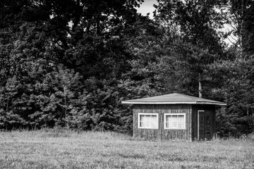 Obraz premium Traditional small wooden scandinavian house at the forest edge. Typical summer cottage. Countryside authentic cozy little cabin in a rural area of brown color with white windows.