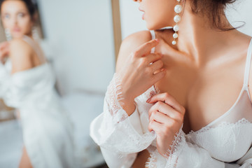 Cropped view of bride in lace bra and pearl earring touching silk robe at home