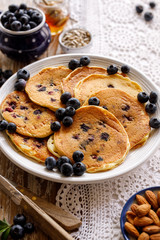 Homemade pancakes topped with fresh blueberries on a white plate on a rustic table close up view