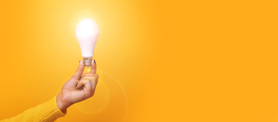 hand holding light bulb, illuminated light bulb, panoramic mock up over yellow background