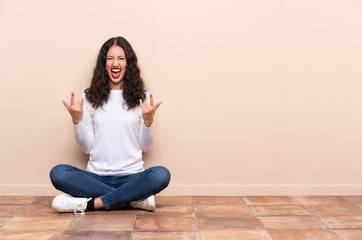 Young woman sitting on the floor making rock gesture