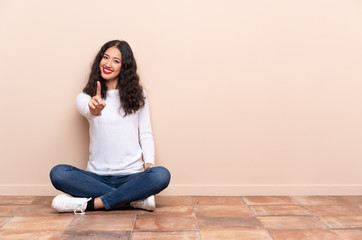 Young woman sitting on the floor showing and lifting a finger