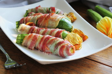 Grilled zucchini fries wrapped in a bacon on white plate