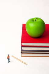 standing miniature man with apple on stack of new books