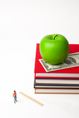 standing miniature man with apple on stack of new books
