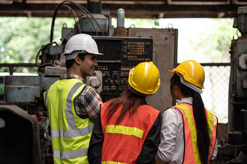 Technician man and factory woman worker discussing about industrial machine application for working in manufacturing plant. They wear helmet or hardhats and vests, gloves for safety working.