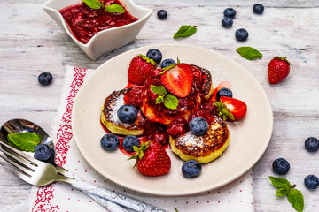 Cottage cheese pancakes with fresh berries and strawberry sauce. Healthy breakfast concept on wooden background