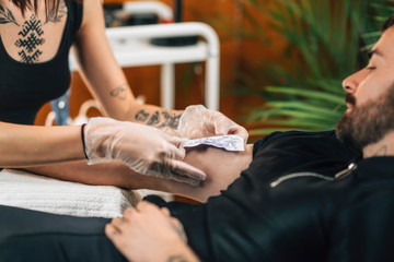 Tattooing.  Female Tattoo Artist Applying Tattoo Stencil onto Male Arm before Tattooing
