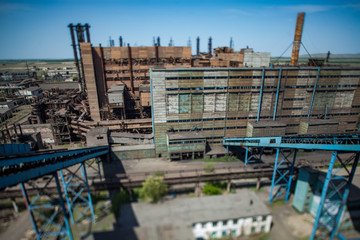 Abandoned soviet metallurgy plant buildings and rusted chimneys on blue sky. Aerial view with tilt-shift effect lens. Partially blurred. Taraz city