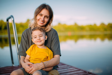 Mother and son hug each other sitting on dock. Summer photography for a blog or advertising about...