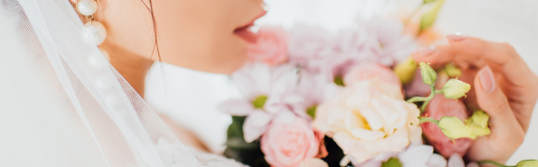 Fototapeta na wymiar Panoramic shot of bride in pearl earring and veil touching bouquet