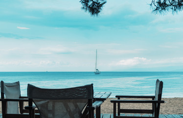 chairs on a tropical beach with a calm sea and a sailing boat in the background