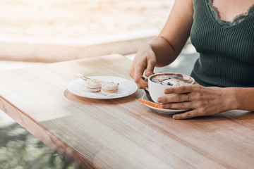 Female hands holding cup of coffee with beautiful latte art on wooden table.