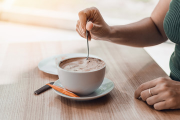 Female hands holding cup of coffee with beautiful latte art on wooden table.