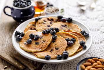 Blueberry pancakes topped with honey and fresh blueberries on a white plate 