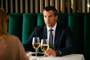 Handsome businessman dressed in the suit drinking wine. Businessman and businesswoman enjoying in the restaurant.