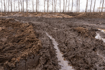 Texture of a dirty bad dirt road dirt road with puddles and clay drying mud with cracks and ruts. Off-road. The background.