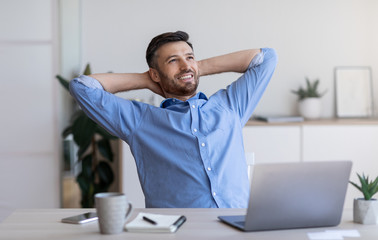 Smiling millennial businessman leaning back in chair at workplace, resting in office